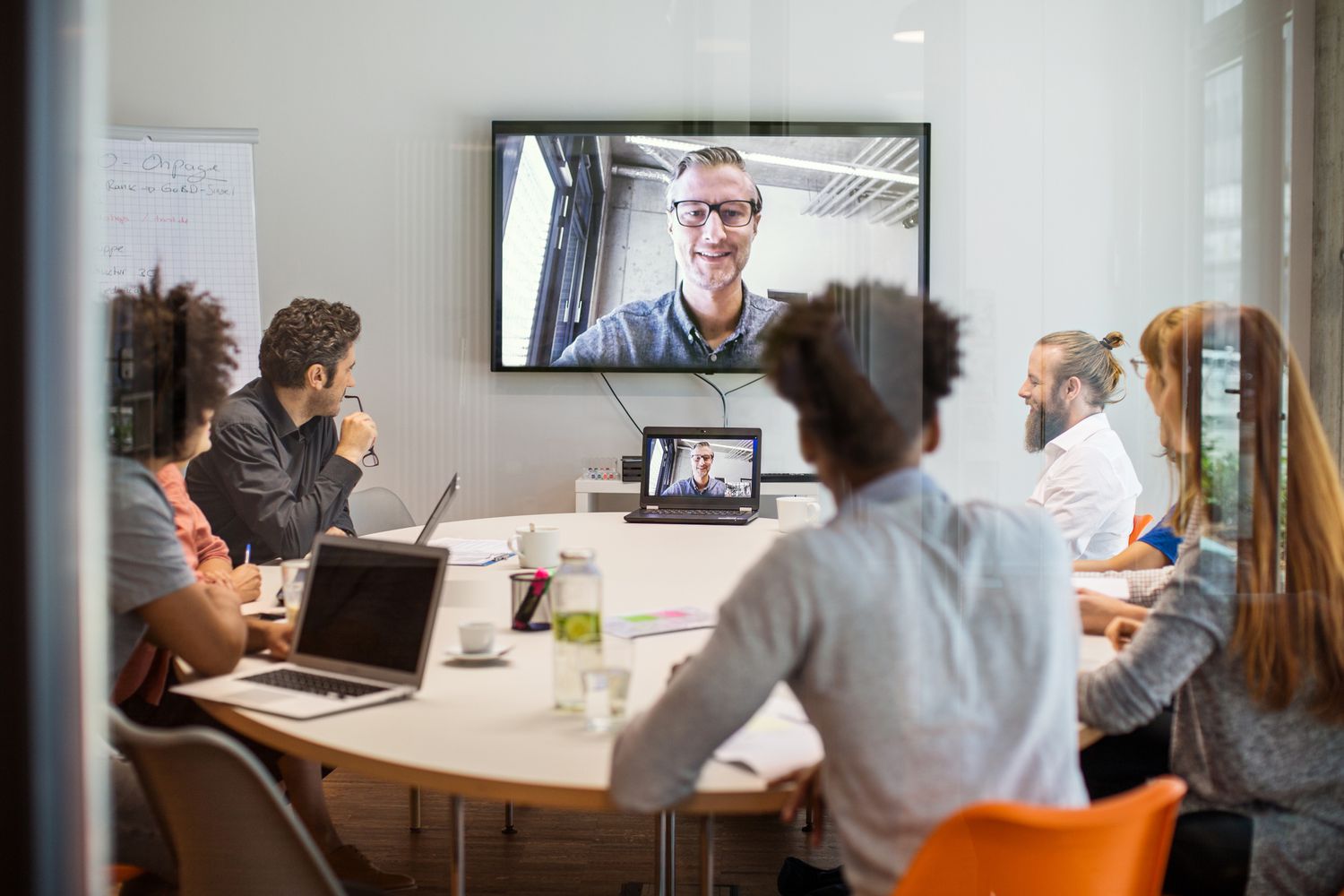 An office conference room with a video conference call on a screen on the wall