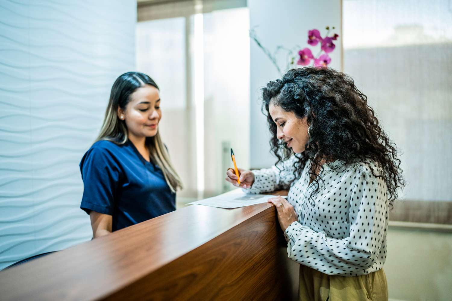 Woman talks with receptionist at dentistâs office reception desk