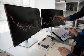 Hands pointing to detail on charts displayed on monitors