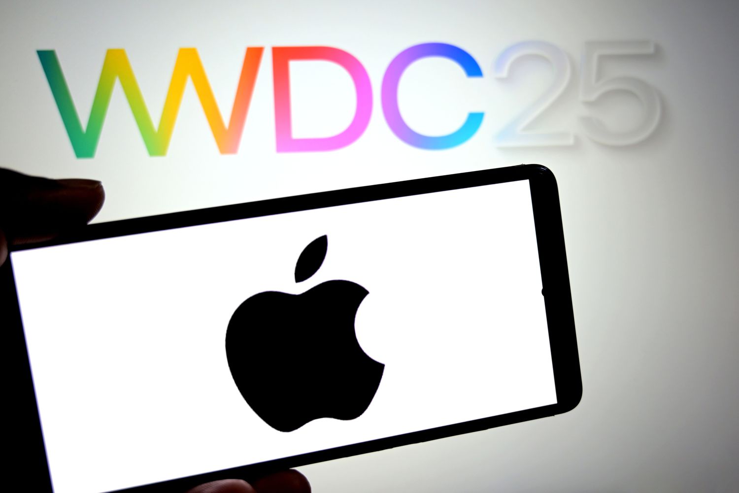 An Apple Logo is seen displayed on a smartphone with a WWDC 2025 logo in the background