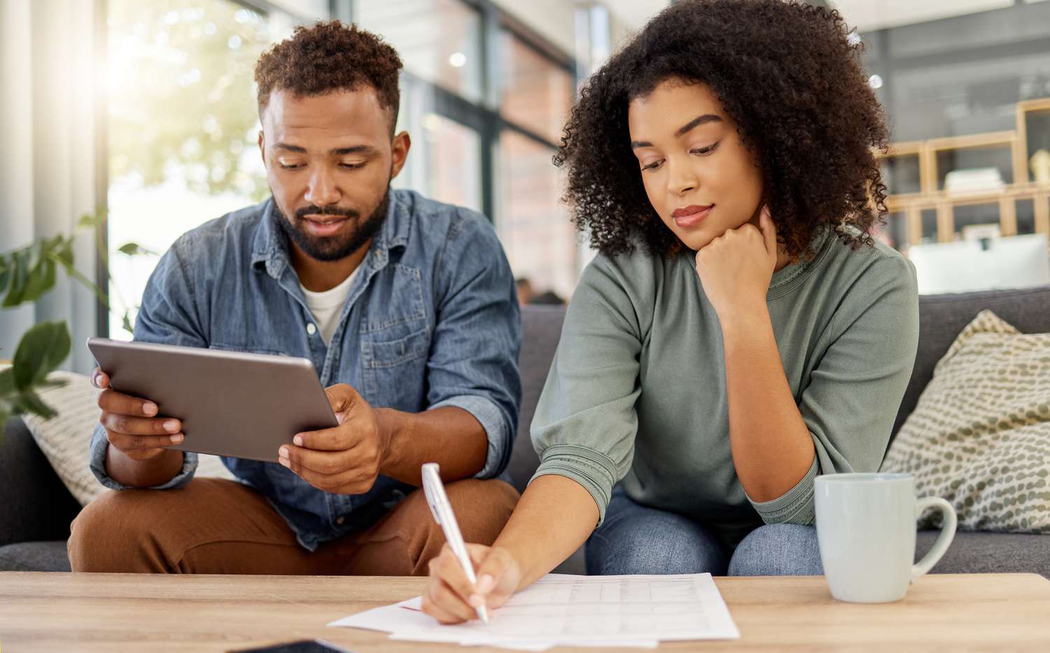 Young couple sitting on their sofa and looking mortgage documents and online mortgage rates and 