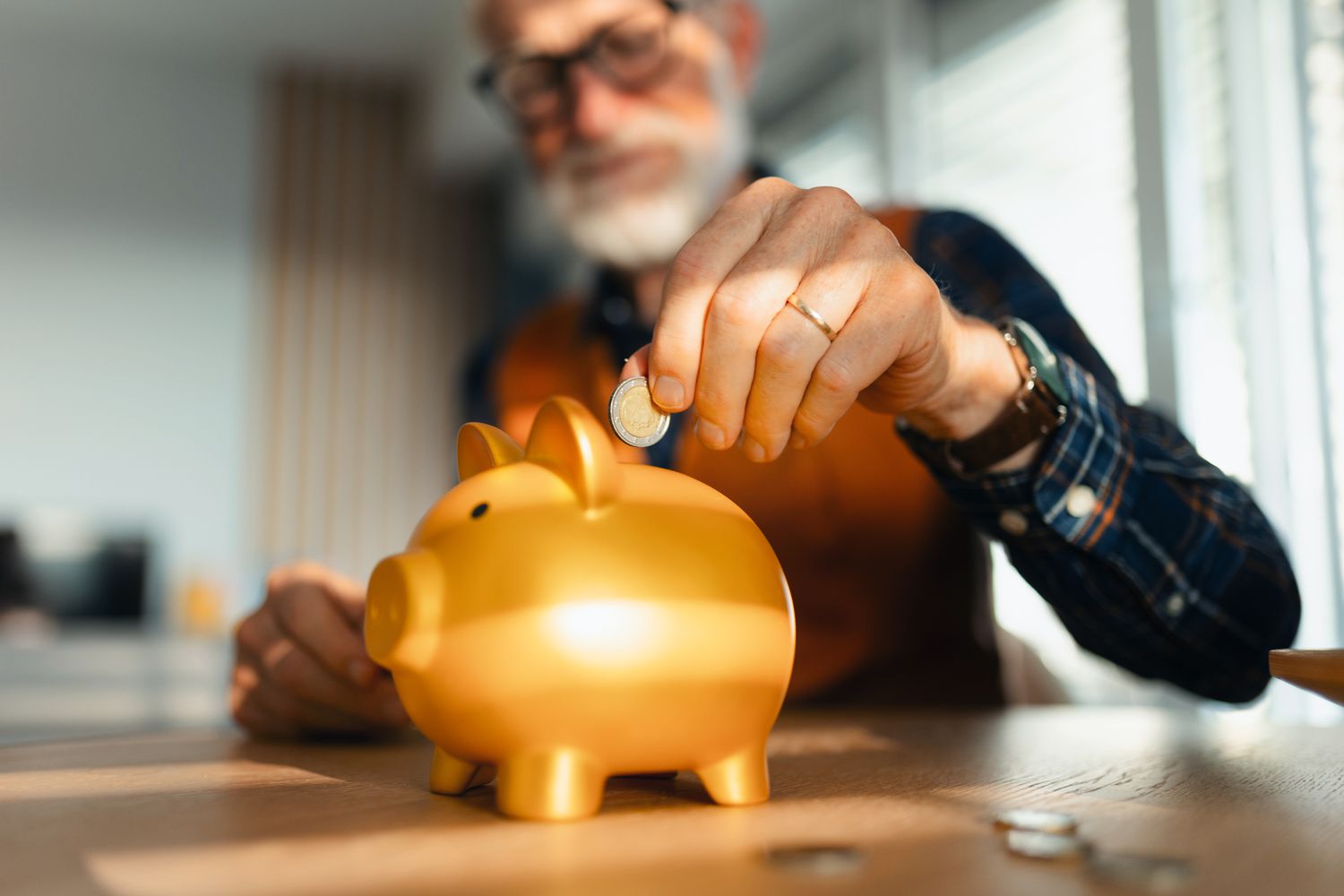 A stock image of a man putting a coin into a piggy bank.