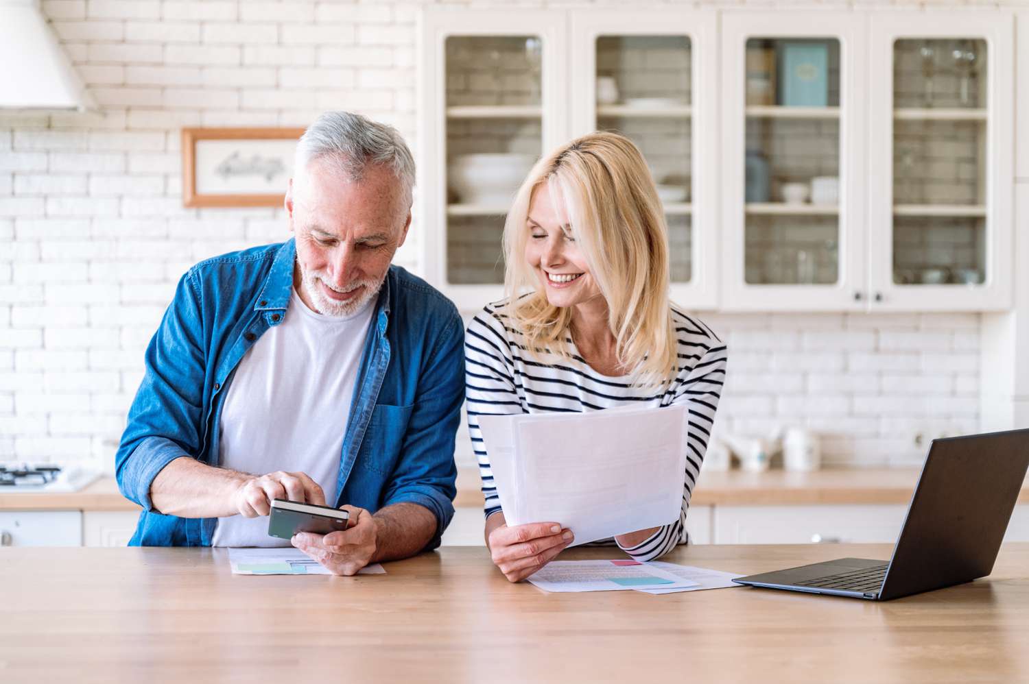 Happy, mature couple managing retirement planning while sitting at their kitchen counter. 