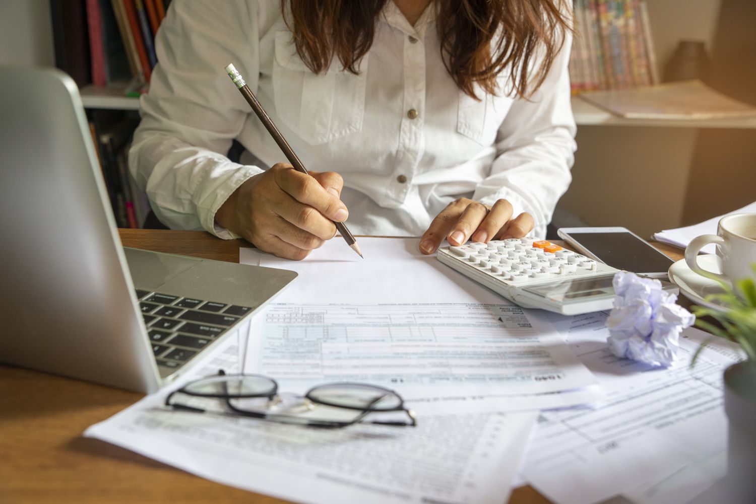Person at a desk using a calculator and laptop to calculate their taxes