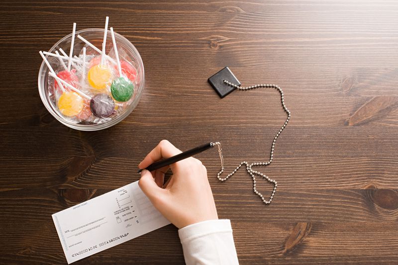 aerial view of a hand holding a pen filling out a bank slip with a bowl of lollipops on the table