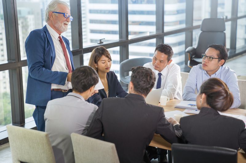 A man addressing a group of young professionals sitting around a table. 