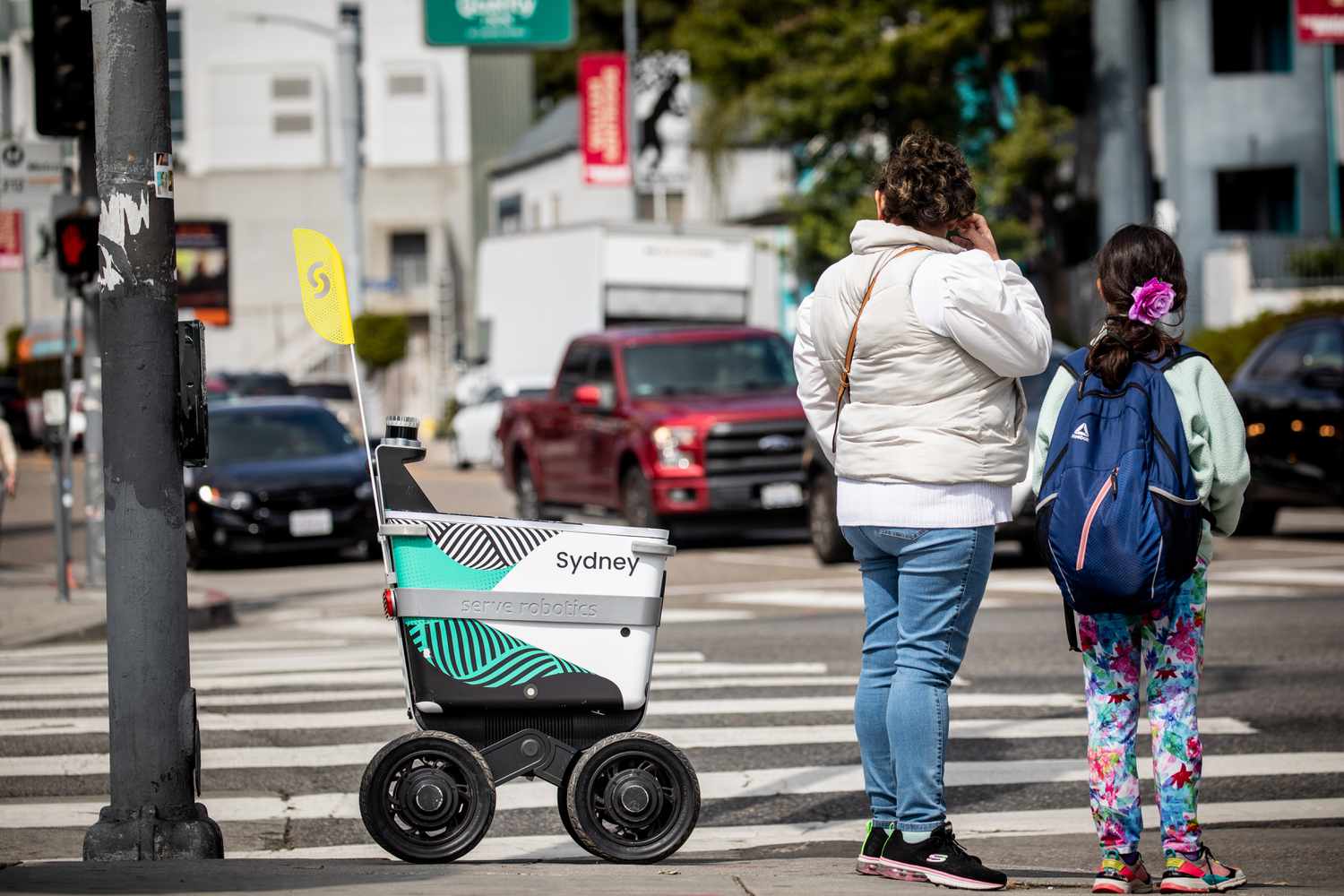 A woman looks at a Serve Robotics delivery robot at a street corner in Los Angeles.