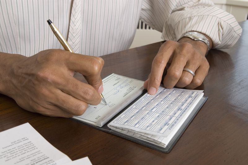 Mid-section of person writing a check in a checkbook