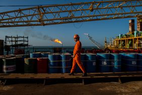 A worker passes stores of oil drums and gas flares while working aboard an offshore oil platform in the Persian Gulf's Salman Oil Field, operated by the National Iranian Offshore Oil Co., near Lavan island, Iran, on Friday, Jan. 6. 2017. 