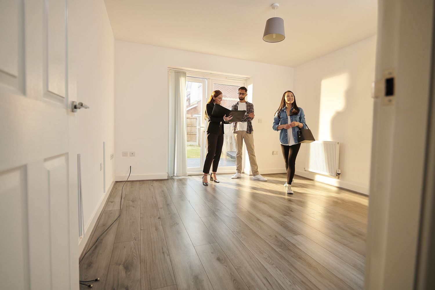 A real estate agent walks a man and a woman through a living room of an apartment