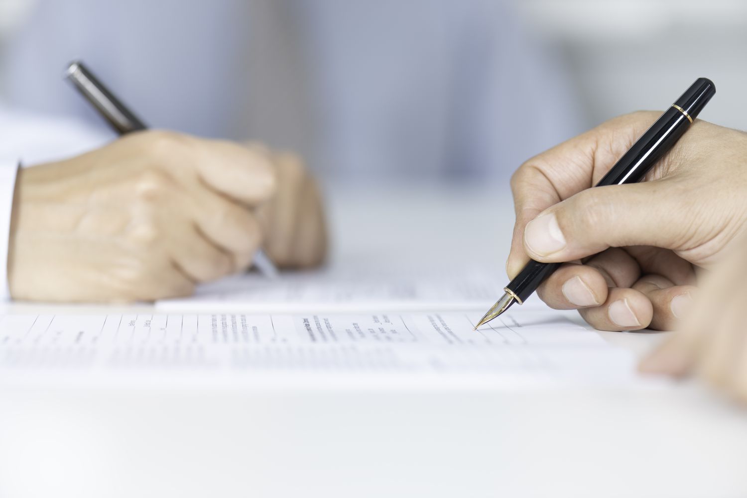 Two representatives from different companies signing with pens resolutions to terms of a business acquisition.