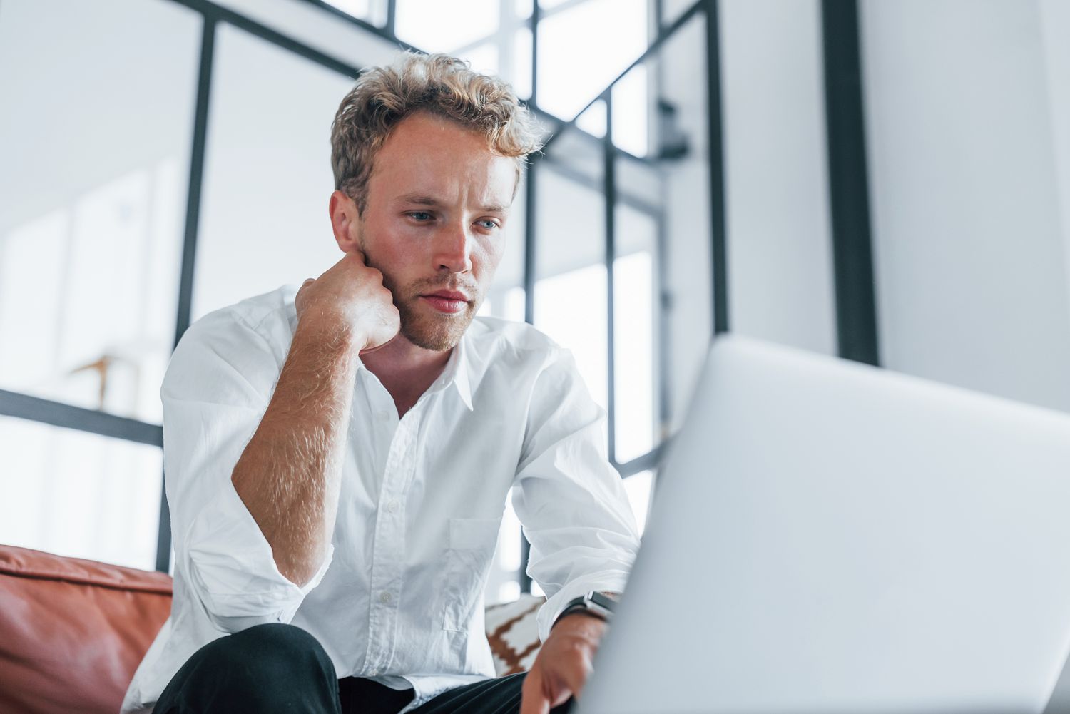 Young man sitting on a couch and looking seriously at something on this laptop