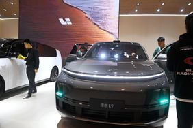 People are seen standing around two electric vehicle on the floor of an auto show.