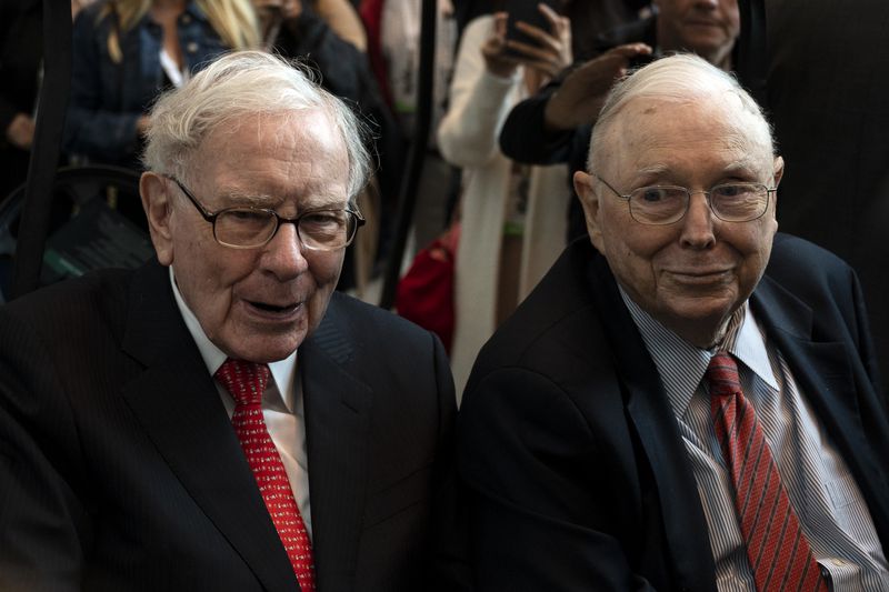 Warren Buffett and Charlie Munger seated together at an event, surrounded by people
