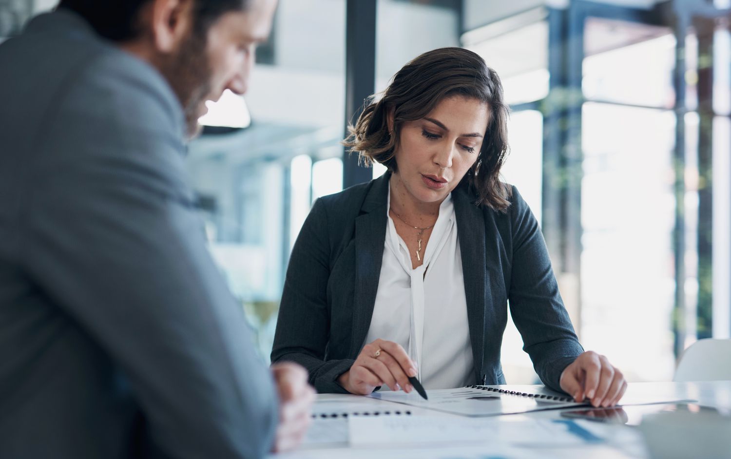 Business professionals review paperwork while sitting in a glass conference room.