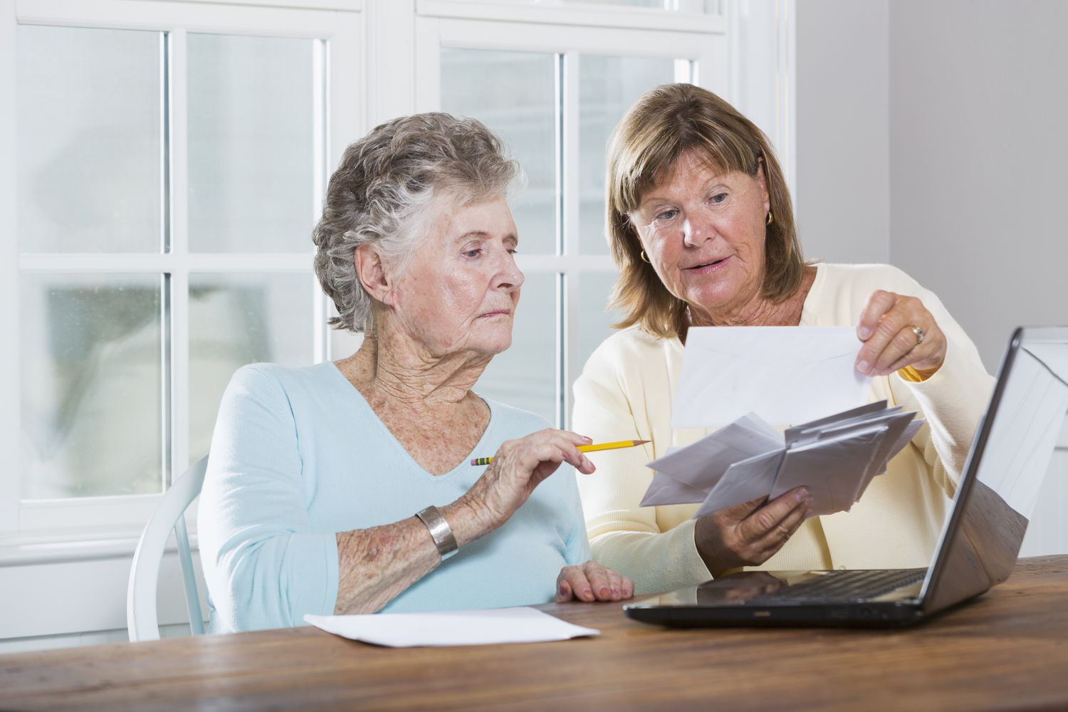 Mature woman (60s) helping elderly mother (90s) pay bills.