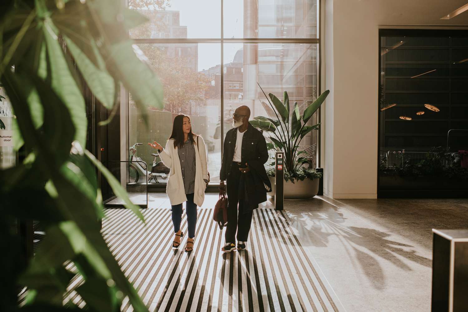 A man and woman enter a large, light filled interior space through rotating doors. 