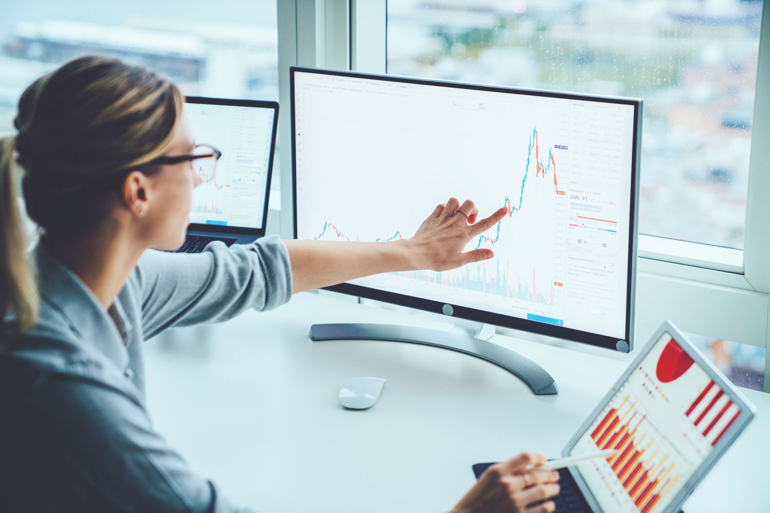 Woman reviewing financial market data on two computer screens in an office