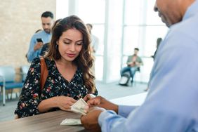 Woman at bank watching bank teller in front of her counting money that she withdrew from her account.