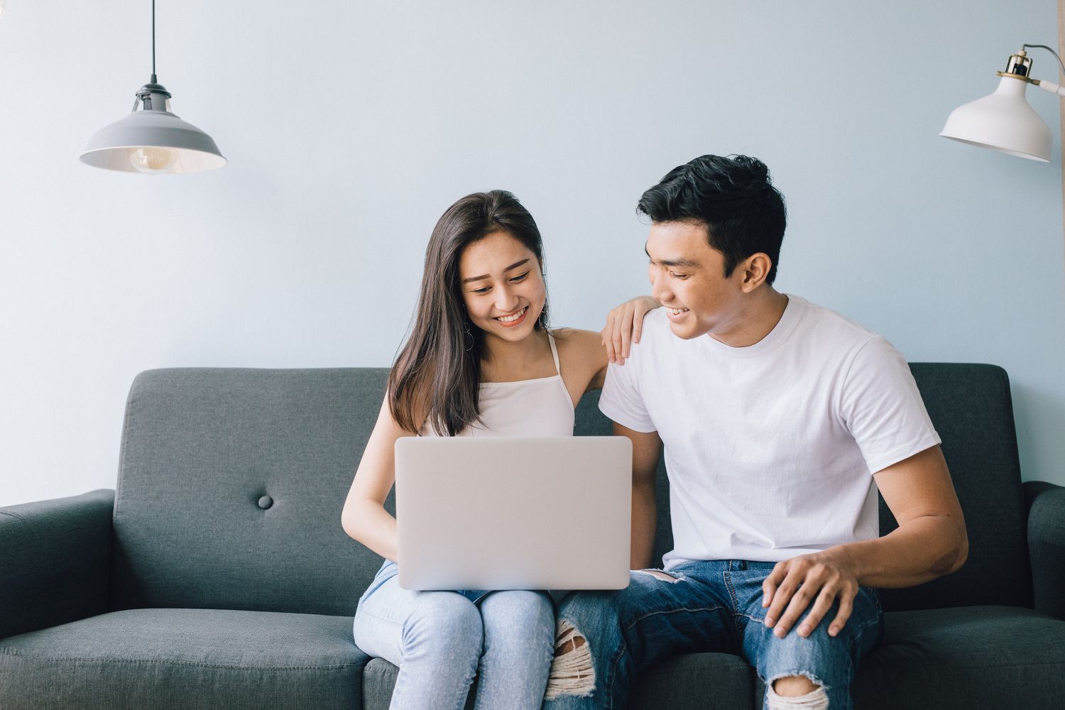 Young couple sitting on sofa looking at laptop and having a laugh