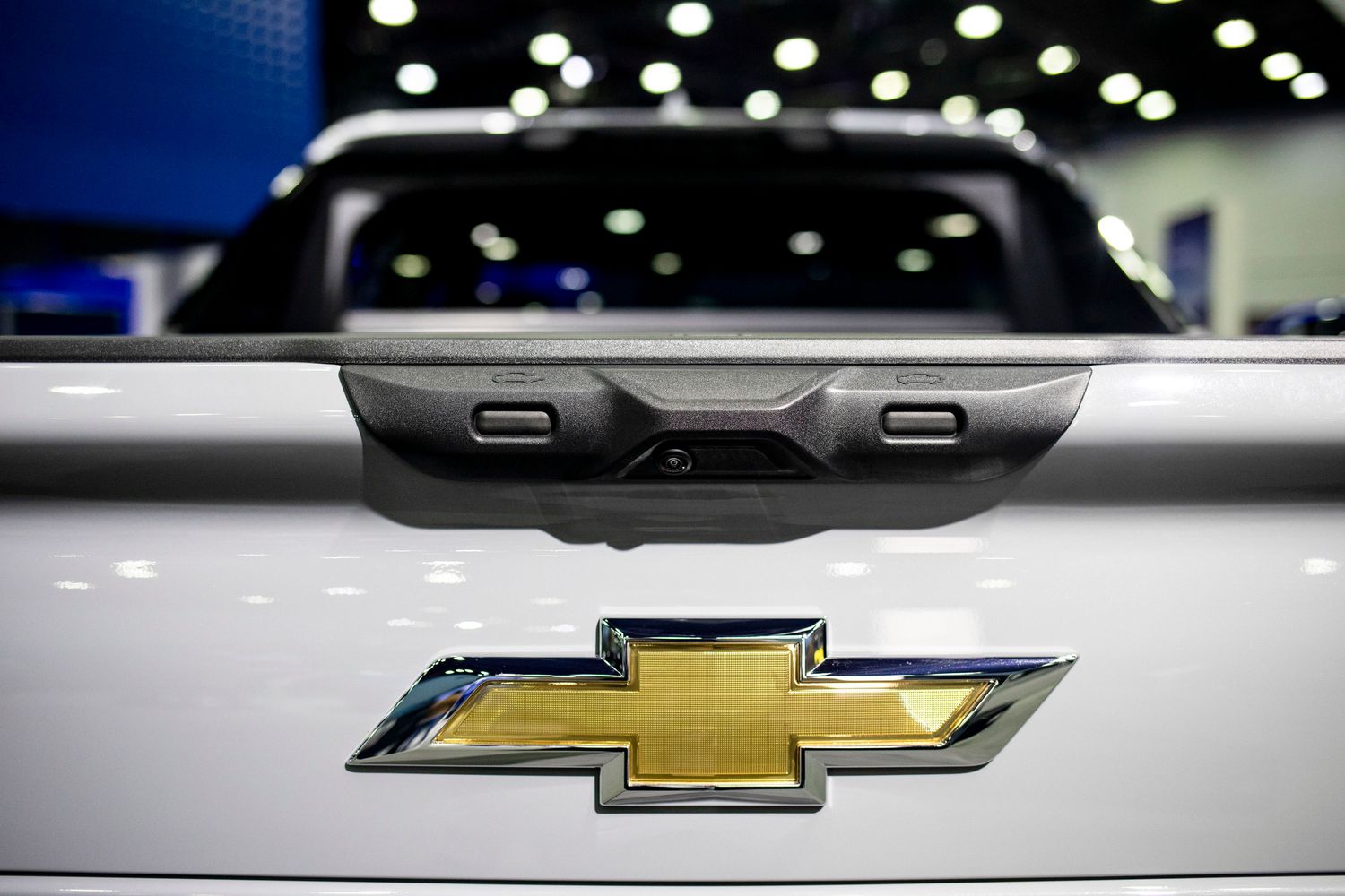 The gold Chevrolet logo is seen on the back of a white pickup truck on the floor of an auto show.