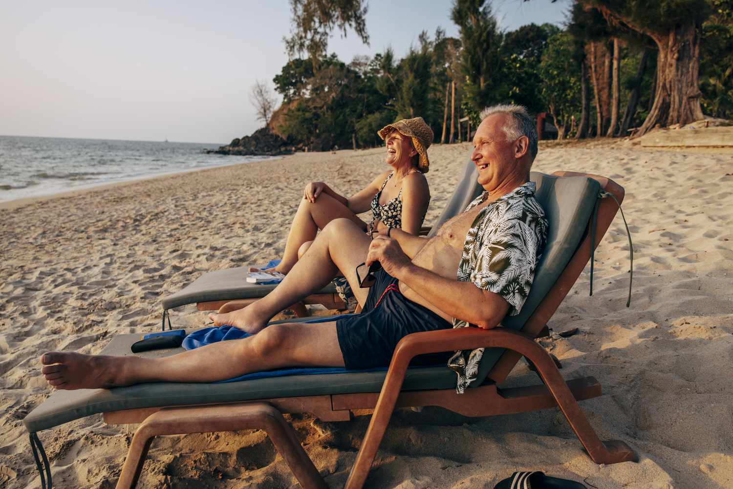 Happy elderly couple sitting on deck chair and enjoying vacation at beach