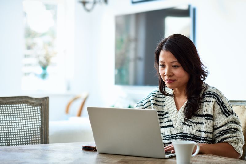A woman uses a laptop at a table with coffee.