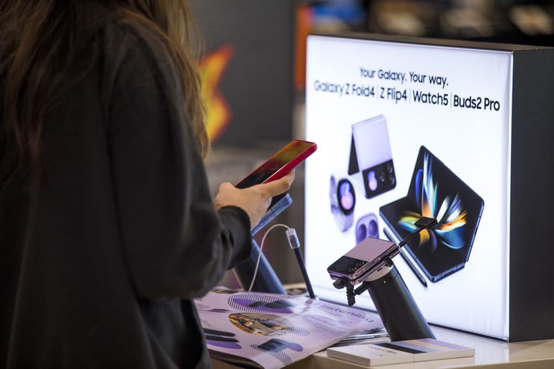 A woman holds a cell phone while standing beside a store display of Samsung smartphones.