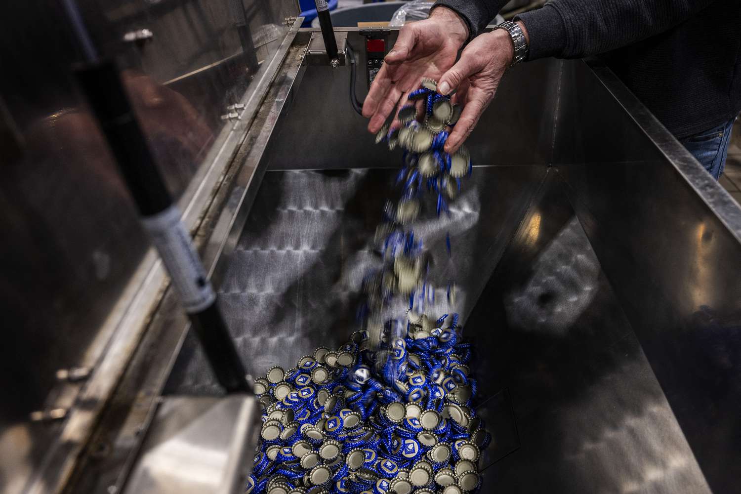 Port City Brewing Company Founder and President Bill Butcher adds bottle caps, which he imports from Mexico, into the bottle machine at his brewery in Alexandria, Virginia, on March 13, 2025. For US craft brewer Bill Butcher, President Donald Trump's expanding range of tariffs have sparked an unexpected impact -- a shortage of bottles to package his beer -- while uncertainty looms over his business costs