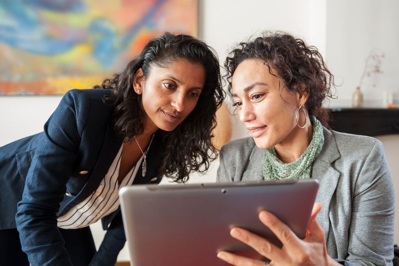 Two business women looking at a tablet computer, discussing a topic.