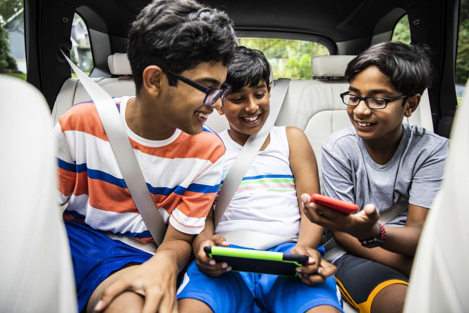 Three tween-aged boys share games on their mobile devices while riding in the family minivan.
