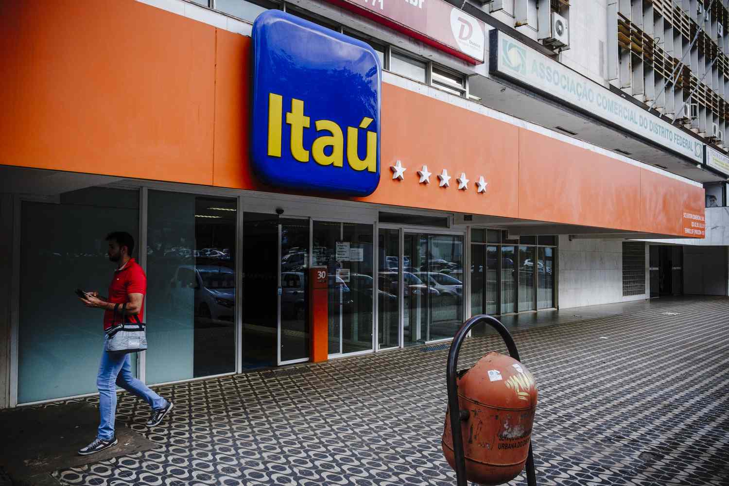 A pedestrian passes in front of a Itau Unibanco Holding SA bank branch in Brasilia, Brazil