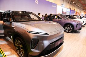 People stand and look at a group of cars at the NIO booth of an auto show in China.
