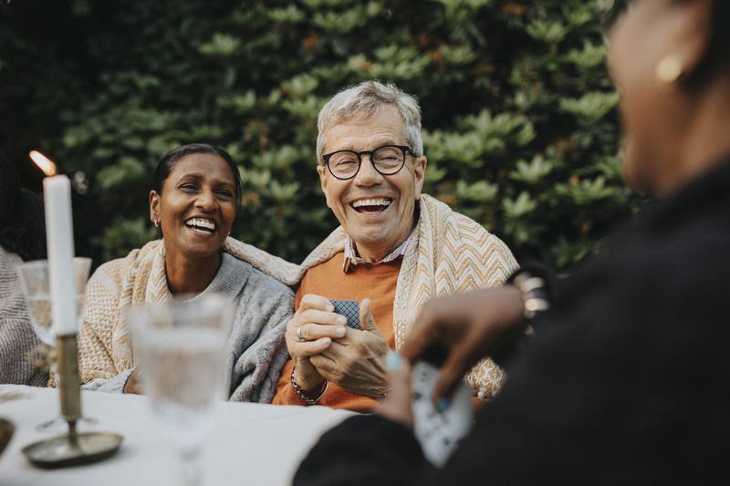 Joyful senior man playing cards at a table with others around him.