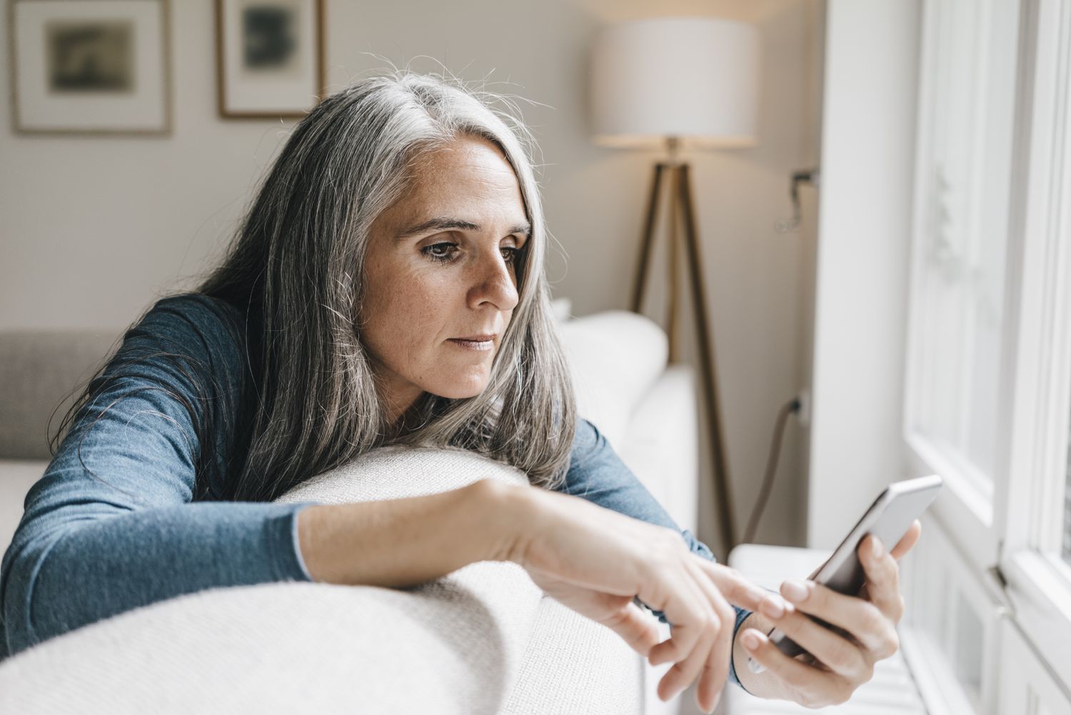 Woman leans on back of couch looking at smartphone in her hand