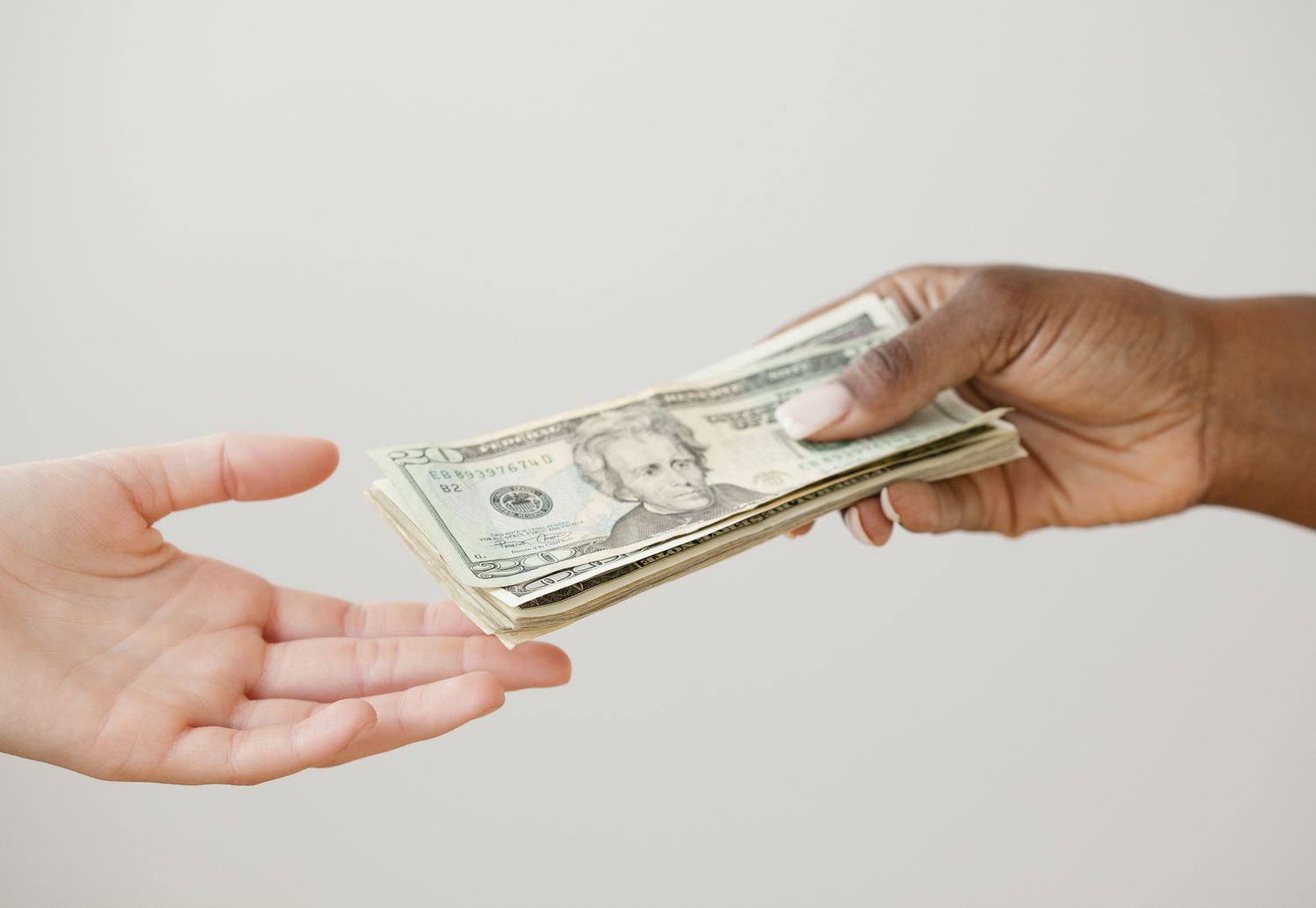 Close up of person's hand handing over a stack of cash to another person's hand