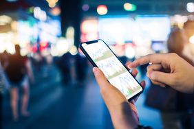 Human Hands Check Financial Stock Charts on a Smartphone in a Busy City Street at Night