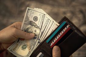Two hands put a sheaf of US $100 dollar bills into a wallet.