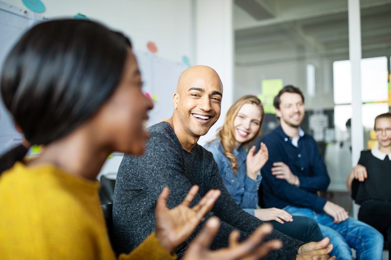 business people smiling in a meeting as one woman talks