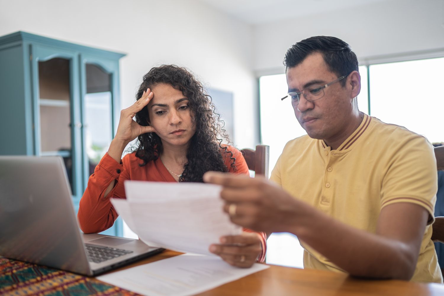 A worried couple sit in front of a laptop, looking at their bills.