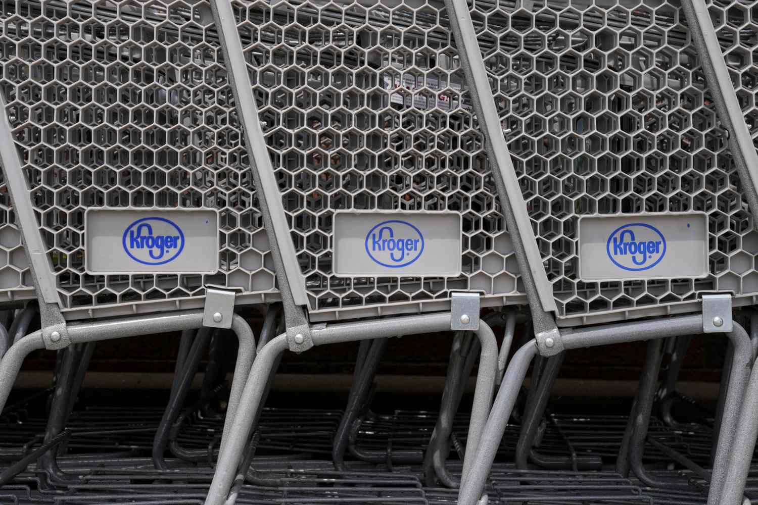 The blue Kroger logo is seen on 3 gray shopping carts that are stacked together left-to-right.