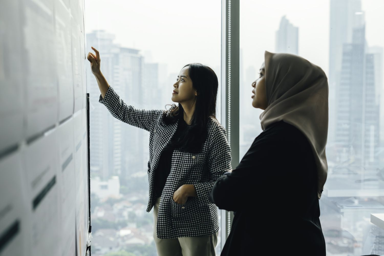 Two women discussing something on a white board.