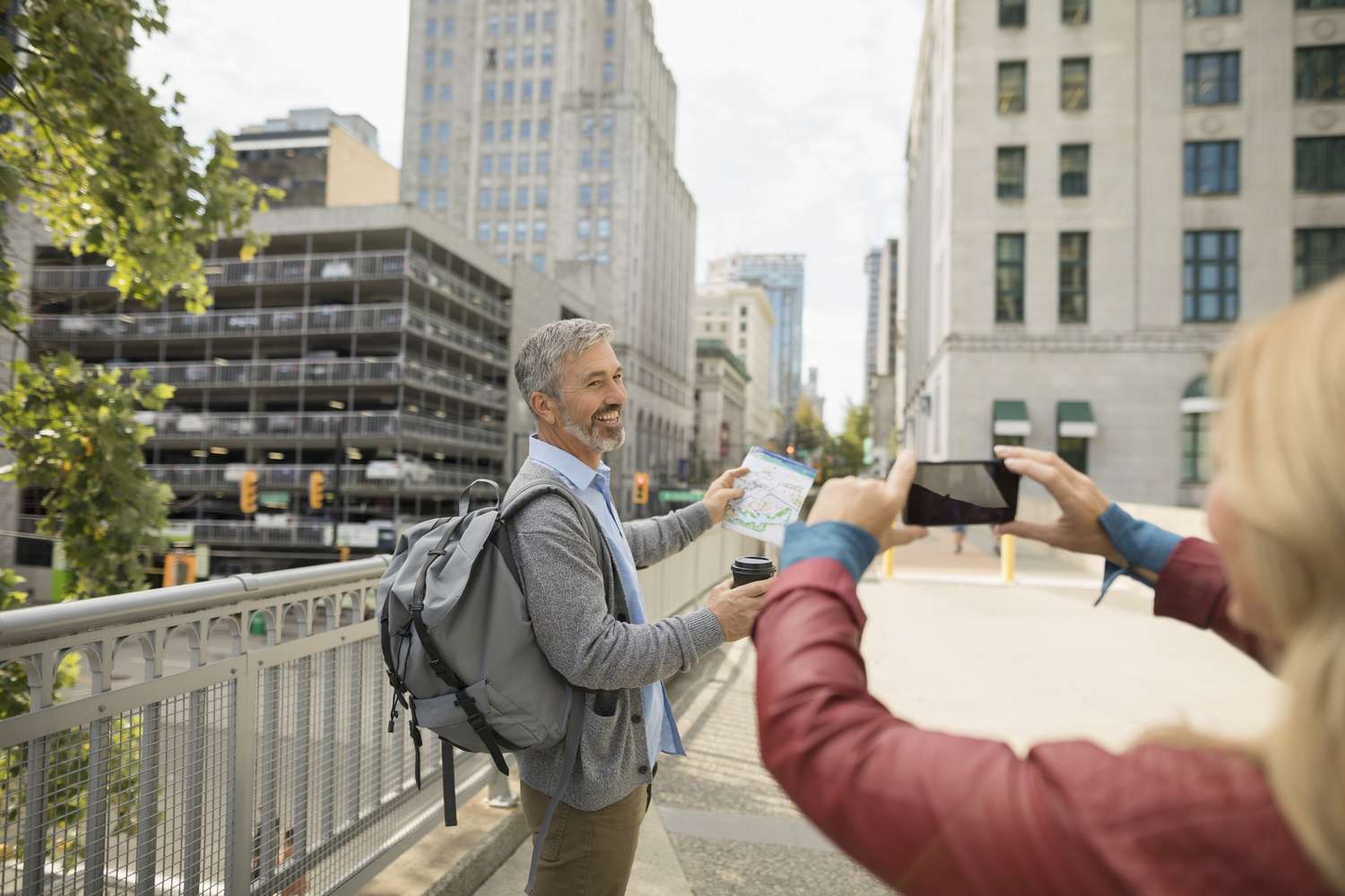 A woman takes a photo of a man on a bridge in a city 
