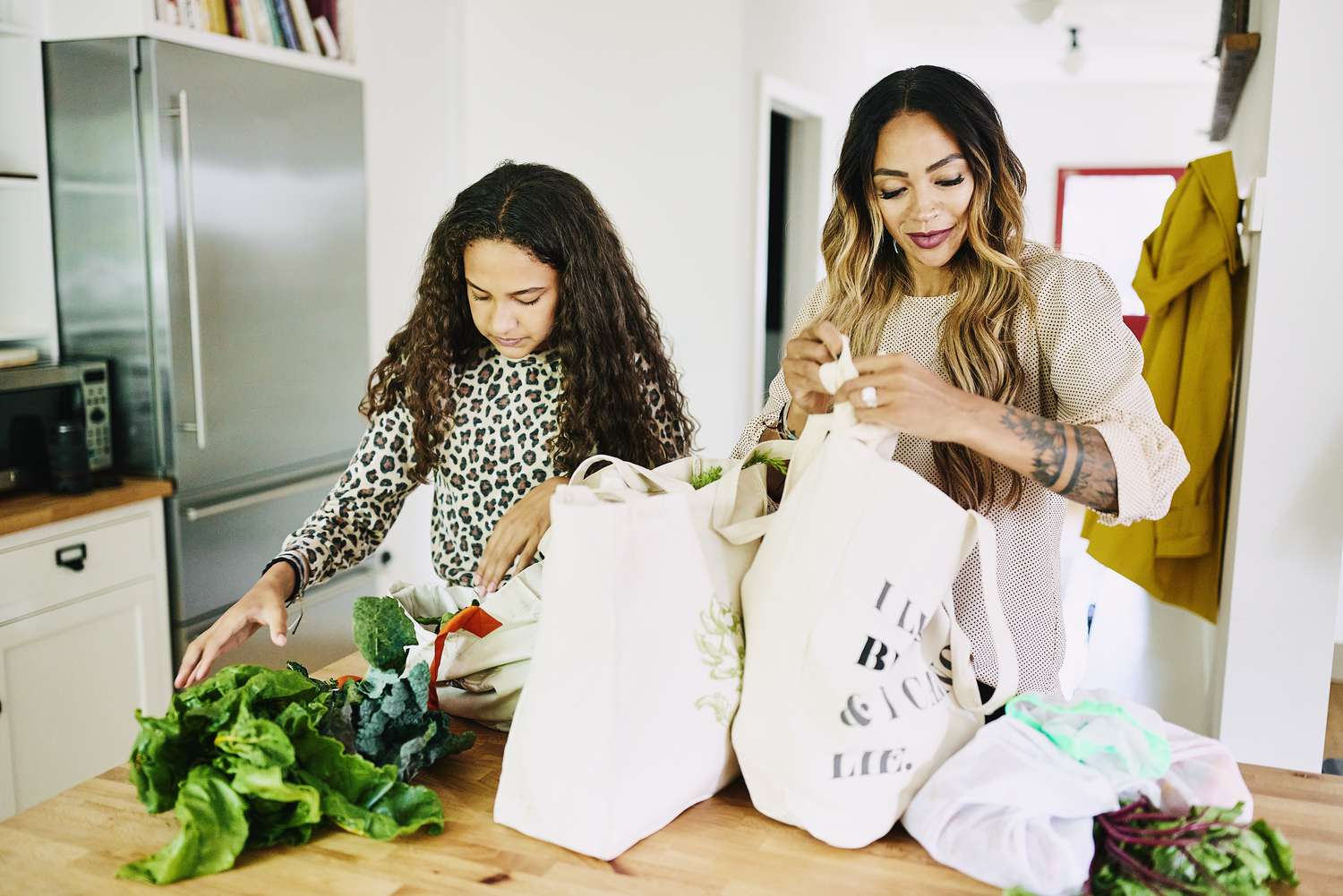 A mother and daughter unload groceries in the kitchen.