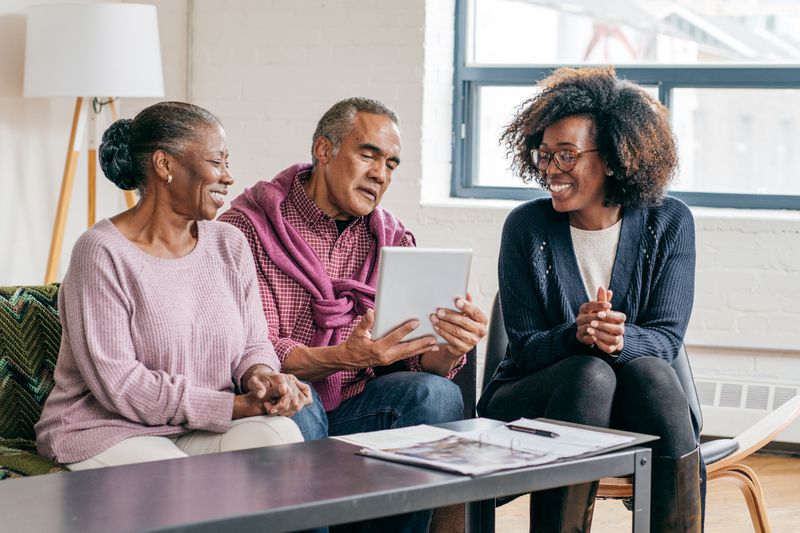 A couple sitting on a couch, talking with their female financial advisor
