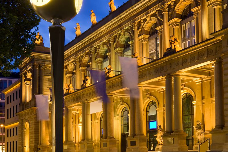 The exterior of the Frankfurt Stock Exchange and a clock at the Borsenplatz are lit for the night.