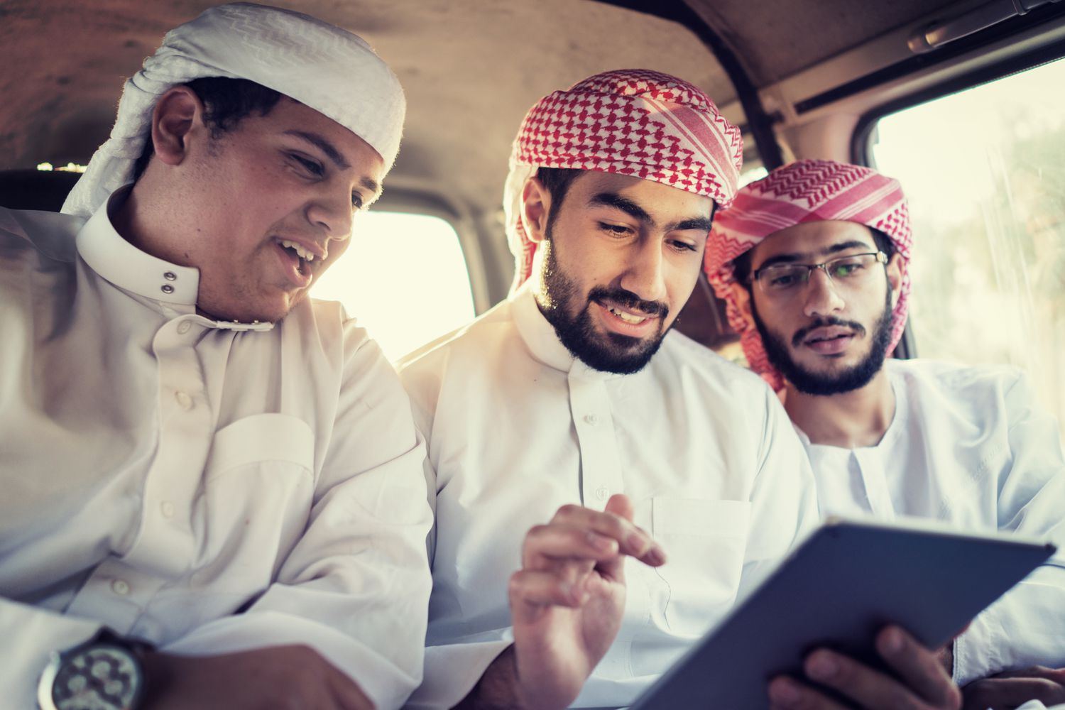 Three young Arab men in a car looking at a tablet