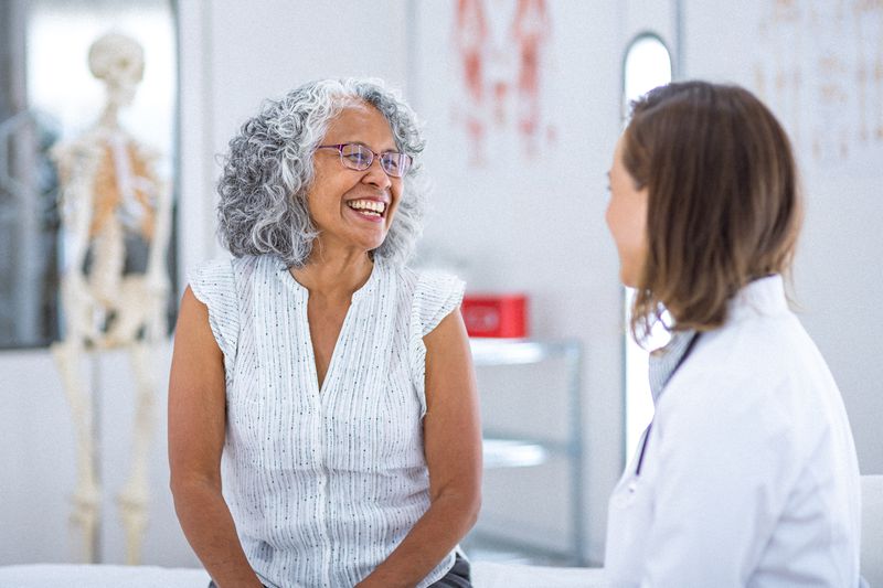 A vibrant and healthy senior woman of Hawaiian and Chinese descent smiles while talking with her female physician during a routine medical appointment.