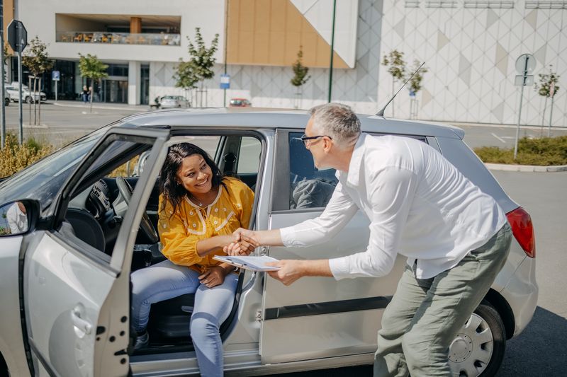 Young adult shaking hands to finalize a car loan to buy car for the first time at a dealer.
