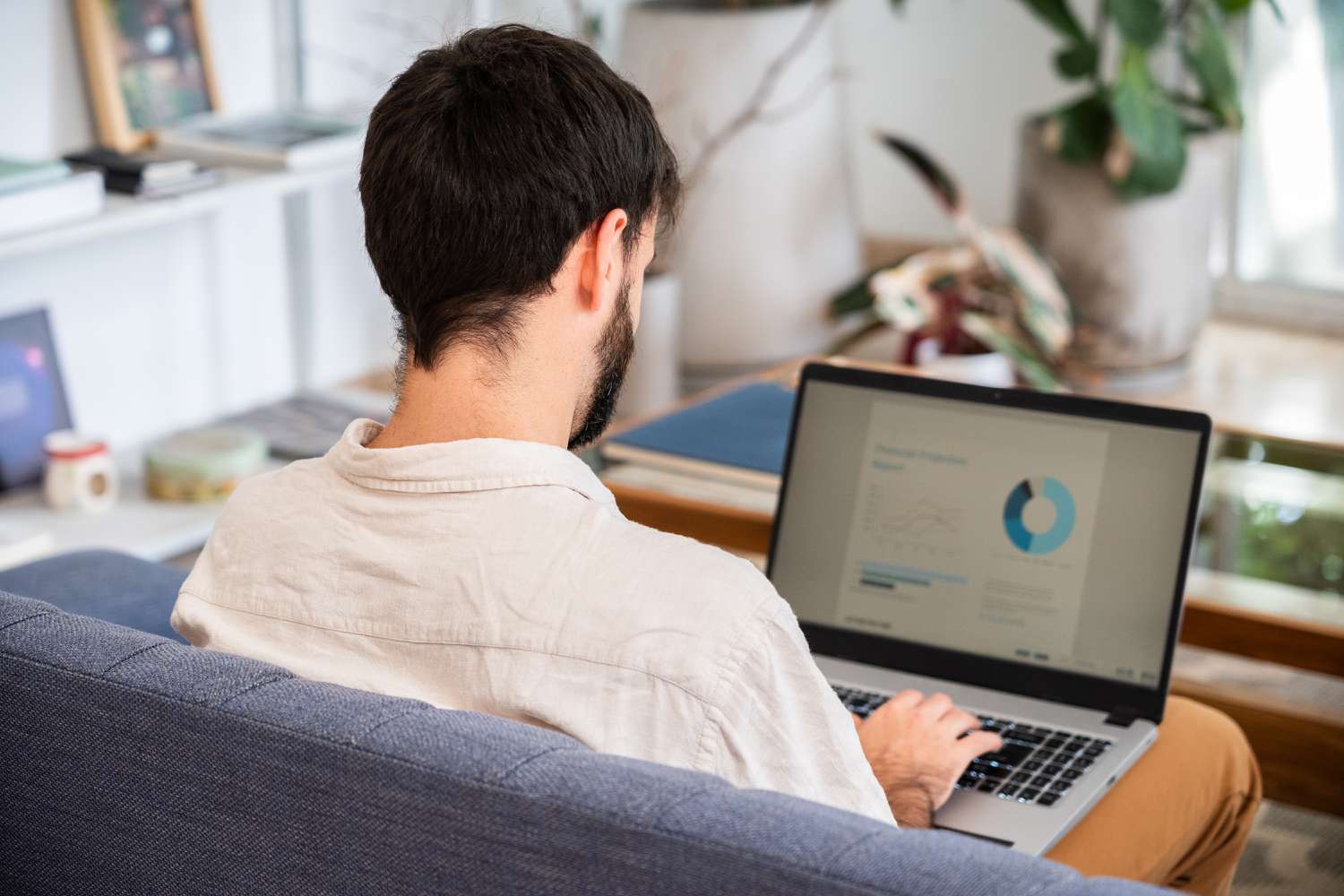 View from behind of a man sitting on a couch and working on a laptop
